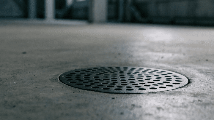 A round cast iron floor drain grate set into a bare basement concrete floor