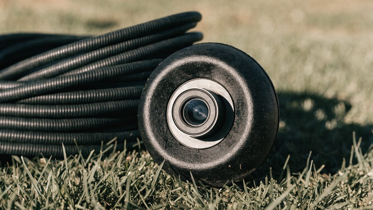 Close-up of a sewer inspection camera head and coiled cable resting on grass