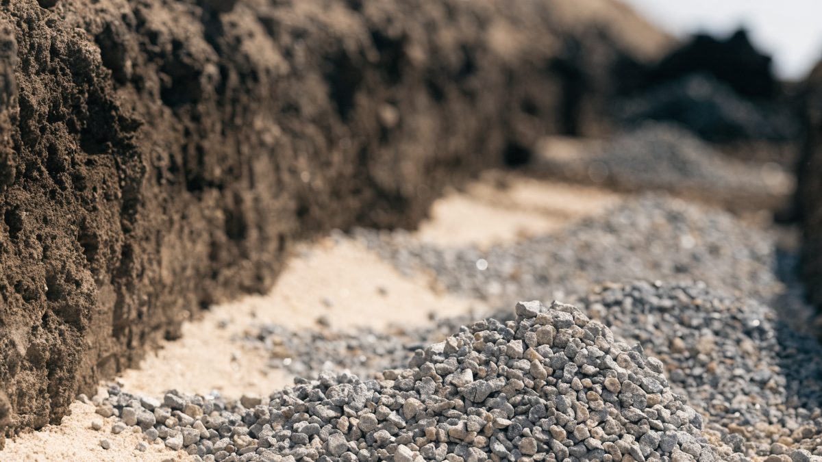 Close-up of exposed pipe bedding and gravel in an open excavation trench