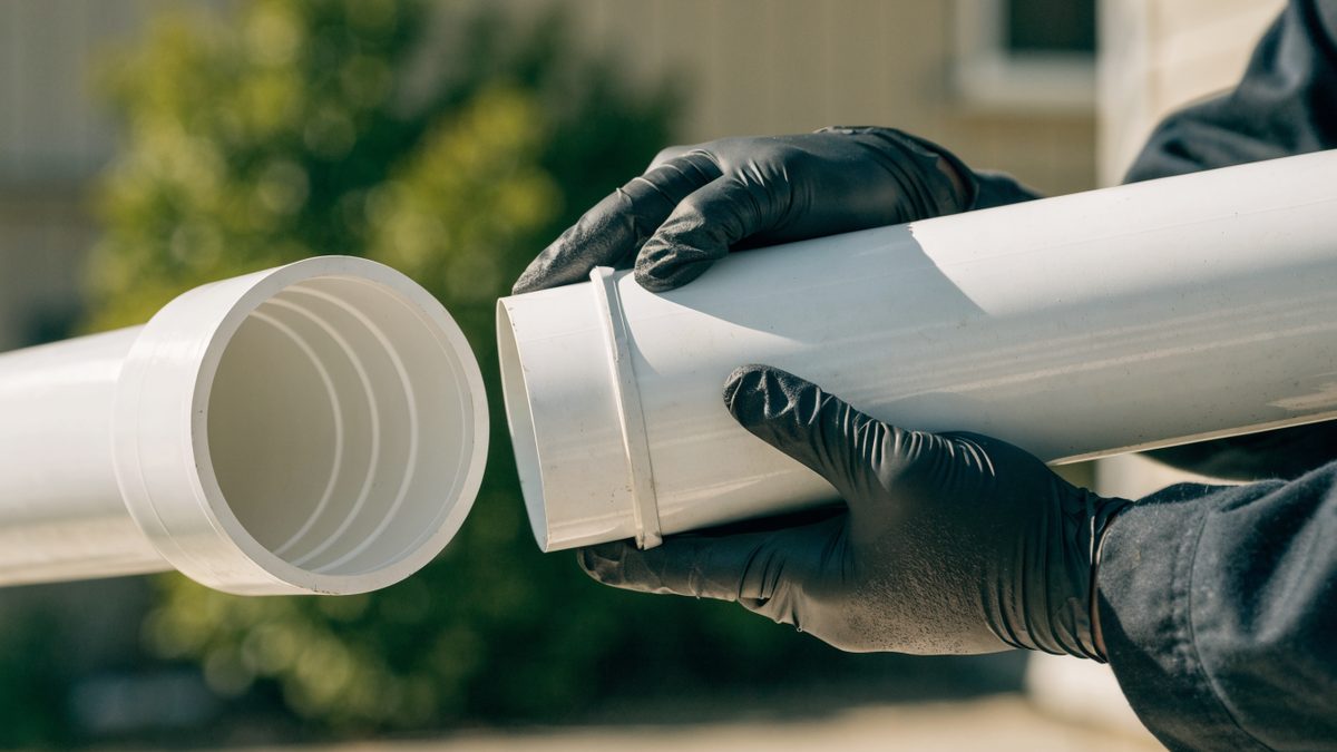 Close-up of gloved hands joining two sections of white PVC sewer pipe
