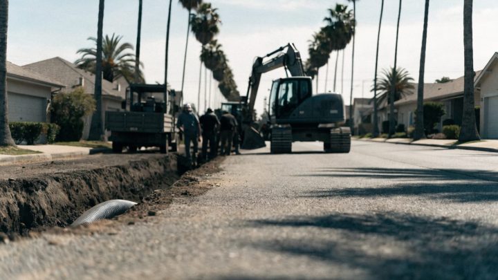 California suburban street lined with palm trees, excavation crew working on a sewer line in the roadway, daytime