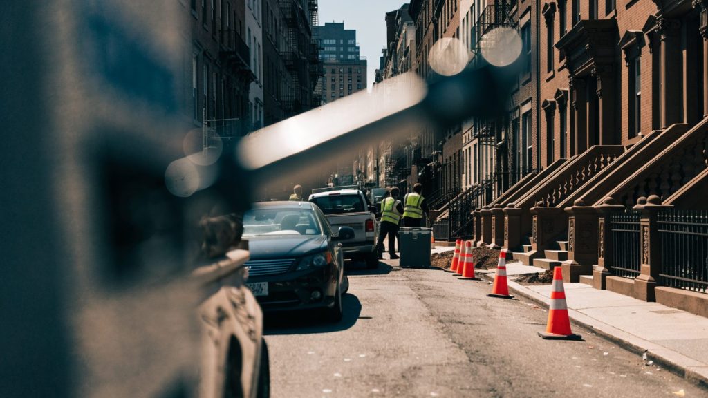 A New York street lined with brownstone buildings, with a utility crew excavating the pavement