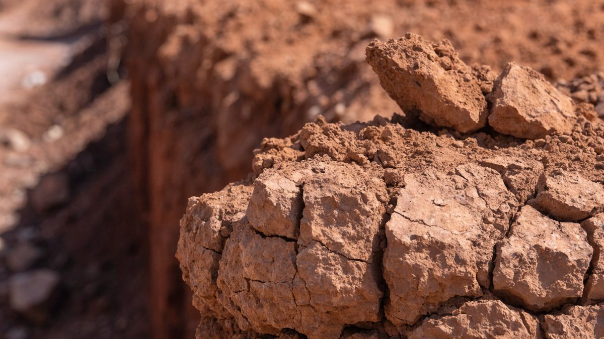 Close-up of cracked reddish-brown clay soil at the edge of an excavation trench