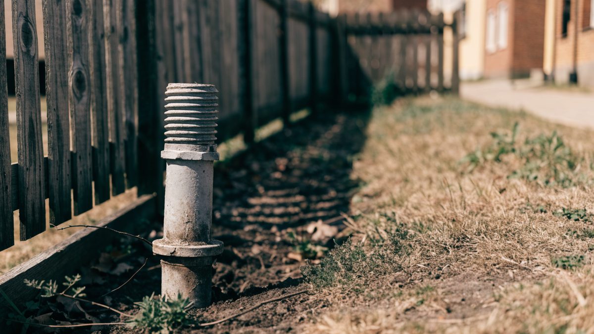 Sewer cleanout pipe positioned near a wooden fence line between two properties