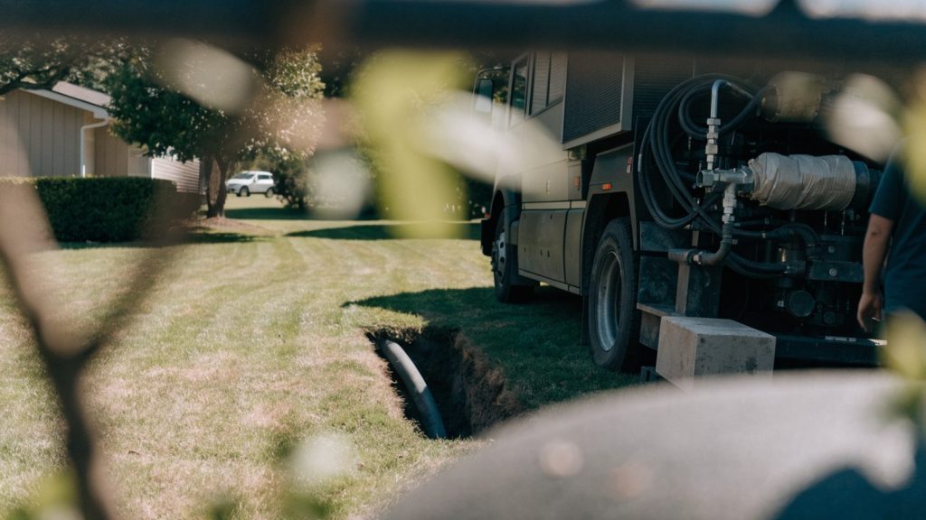 A trenchless pipe repair truck beside a small access pit dug in a residential yard